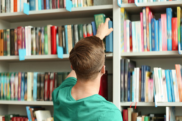 Young man taking book from shelving unit in library