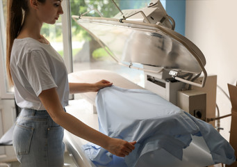 Female worker using ironing press in dry-cleaning