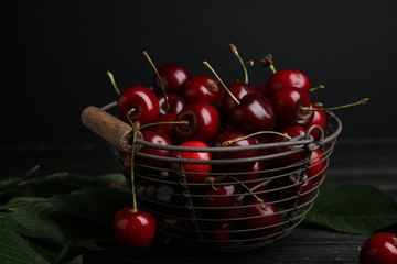 Metal basket with ripe sweet cherries on dark wooden table