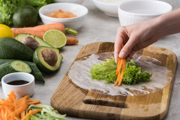 cropped view of woman putting cut carrot on lettuce, on cutting board