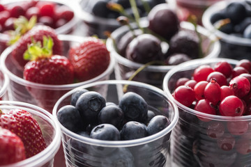 selective focus of cranberries, strawberries, blueberries and cherries in plastic cups