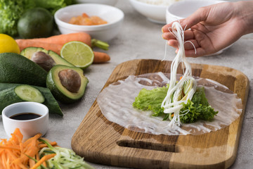 cropped view of woman putting noodles on lettuce and rice paper on cutting board