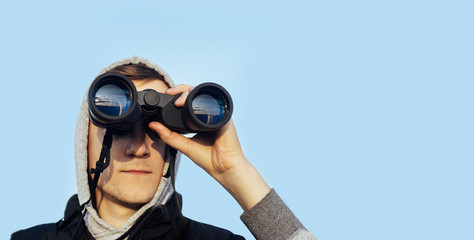 A man with modern binoculars against the sky and green hills. The concept of hunting, travel and outdoor recreation. Banner with  copy space.