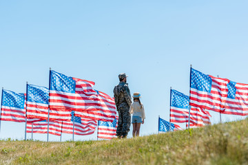 man in military uniform standing with daughter near american flags - Powered by Adobe