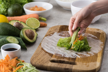 cropped view of woman putting cut cucumber on carrot, lettuce and rice paper