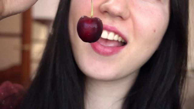 Young brunette woman eats red sweet cherry. Close-up.