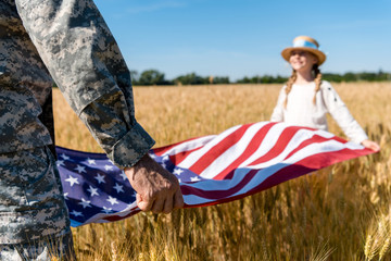 Cropped view of man in military uniform holding American flag with daughter in field