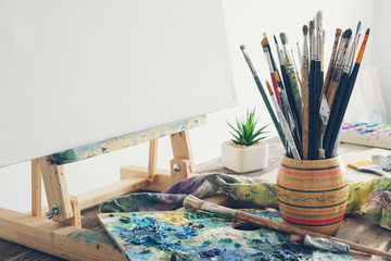 Artistic equipment in studio: canvas on wooden easel, paint brushes, paints and used palette.  Copy space for text.