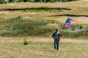 handsome military man in uniform walking and holding american flag in summertime