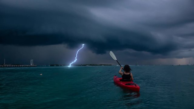 Adventurous girl on a red kayak is kayaking towards a thunderstorm during a dramatic sunset. Taken in Key West, Florida Keys, United States. Still Image Continuous Animation
