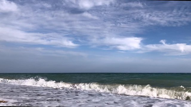 Waves of the Mediterranean in Turkey in the evening. A coastline with pebbles. A look at the horizon of a green sea and a blue sky with white clouds. A lot of text space below. The concept of tourism 