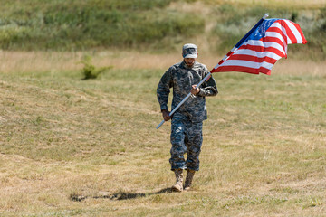 selective focus of soldier walking and holding american flag in summertime