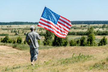 military man in uniform walking on grass and holding american flag
