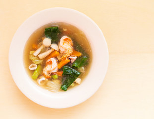 Seafood soup with prawn squid and vegetable in bowl on wooden background.