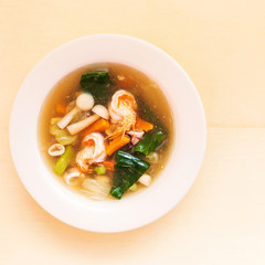 Seafood soup with prawn squid and vegetable in bowl on wooden background.
