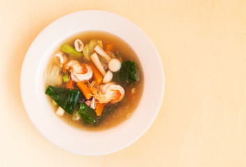 Seafood soup with prawn squid and vegetable in bowl on wooden background.