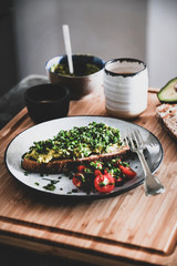 Healthy vegan summer breakfast. Avocado toast on sourdough bread with chives, coriander and cherry-tomatoes with cup of coffee on wooden board. Vegetarian, dieting, alkiline diet, clean eating concept