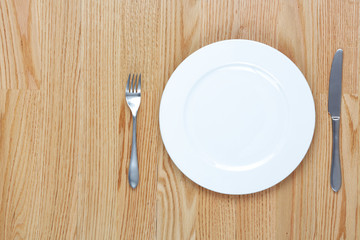 Dining fork and knife beside a plate on a wood table with copy space