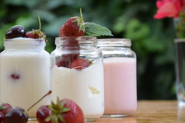 Healthy breakfast - granola, strawberries, cherry, honeysuckle berry, nuts and yogurt in a bowl. Vegetarian concept food. Top view. pudding or cocktail on the background of green foliage