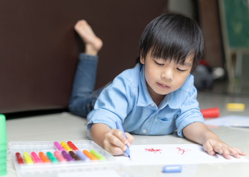 asian little boy is writing homework on floor at home.Asian child using a colorful pencil drawing picture on white paper.