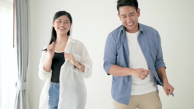 Happy Asian couple dancing together at home, slow motion.