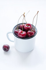 Berries of ripe cherry in a white metal mug on a white background. Country style