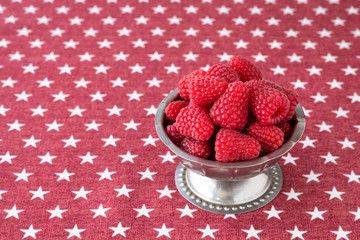Luscious fresh picked raspberries in a stainless steel cup on a background of white stars on a field of red