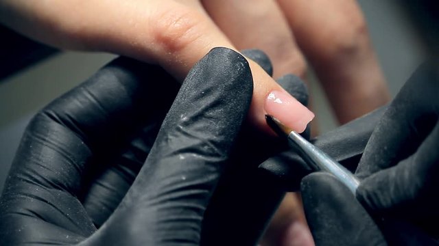 A professional nails care in process, cosmetician in black gloves making nails female customer for a manicure with polygel cover