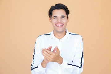 Portrait of enthusiastic guy applauding against beige wall. Happy handsome young man clapping hands in excitement. Success concept