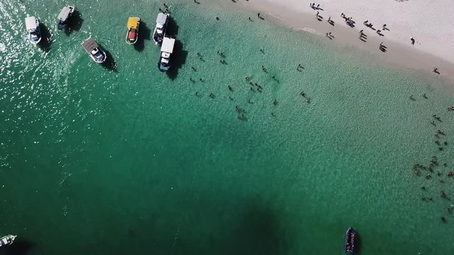 Drone view of people inside the blue ocean, and some boats in a tropical beach Pontal do Atalaia, Arraial do Cabo, Rio de janeiro