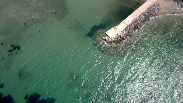 Aerial view of turquoise small beach with a pier in the area of Agia Paraskevi Halkidiki, Greece, up and forward movement by drone