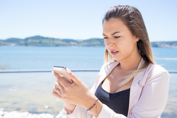 Frowning confused user holding smartphone and staring at screen. Puzzled young woman in casual...