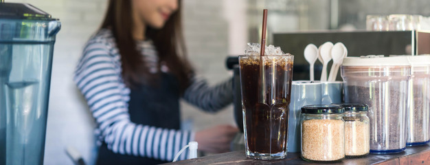 Ice americano on coffee counter with young business owner working in background, dimension image...