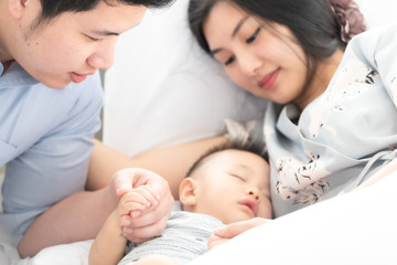 Obraz premium Family of 8 months old baby sleep in bed hold hands with mom and dad together