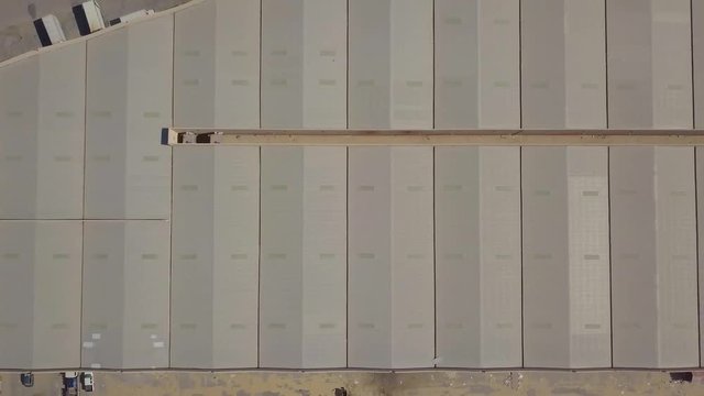 Vertical birds eye view zoom out reveal of many storage facility warehouses side by side in the desert with trucks (4K)