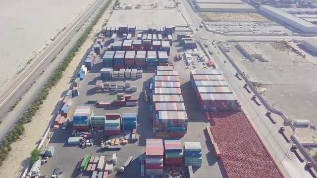 Reveal of a very large container yard with colorful containers and highways on either side in the desert (4K)