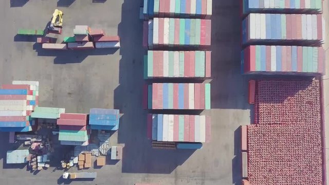 Large yard with stacked containers while a container carrier lifts a container and a truck is parked (4K)
