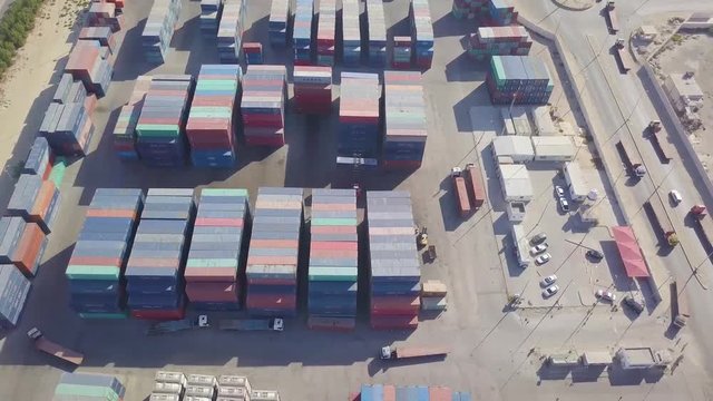 A fleet of trucks enter the massive container yard with colorful containers and loaders getting ready to be loaded with cargo (4K)