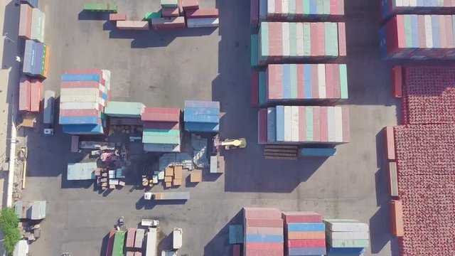 Vertical pan of a very large gated container yard with trucks, a forklift, and a cargo carrier (4K)