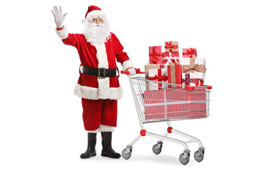 Santa claus standing with a shopping cart full of presents and waving