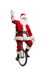Cheerful santa claus riding a unicycle and waving at the camera