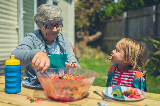 Toddler and grandmother eating lunch at table outdoors