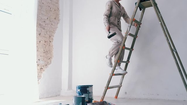 girl climbing a ladder with paint roller in hand getting ready to paint the wall