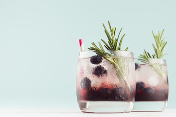 Fresh arctic liquors with ice cubes, blueberry, rosemary, straw in two glasses on white wood table...