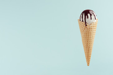 White ice cream in crisp waffle cone with chocolate sauce on pastel green background, mock up, summer food.