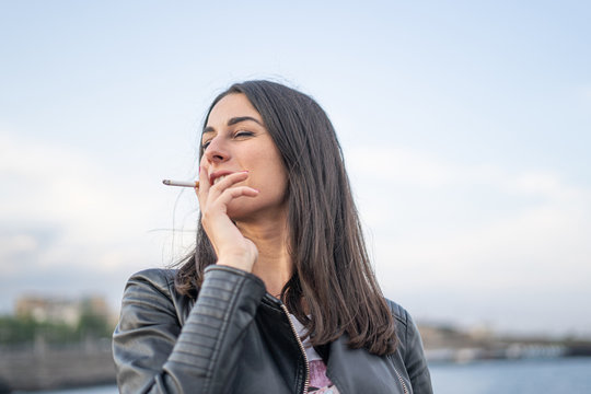 Young woman with a leather jacket smoking a cigarette outdoors