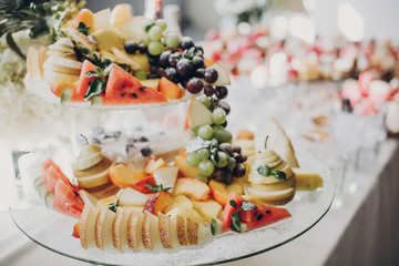 Delicious fruits appetizers, desserts on stand, modern sweet table at wedding or baby shower. Luxury catering concept. Fruit bar at wedding reception, melon,watermelon,grapes,pear slices
