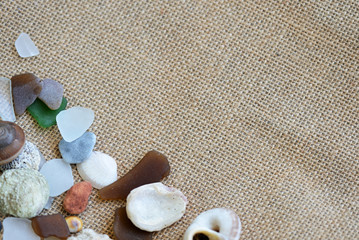 Sea glasses, shells and stones on a rough woven background close-up. Vacation concept