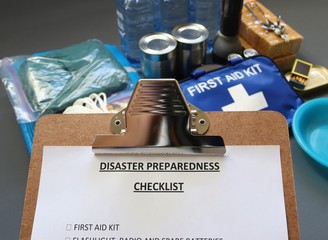 Disaster preparedness checklist on a clipboard with disaster relief items in the background.Such...