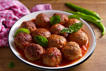 Meatballs in tomato sauce, garnished with basil in bowl on wooden table
